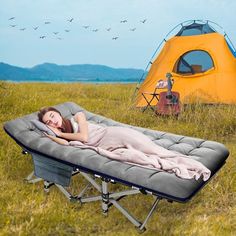 a woman laying in a bed on top of a field next to a yellow tent