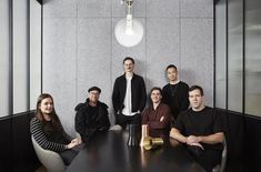 a group of people sitting around a black table in an office setting with a light hanging over it