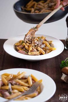 pasta with mushrooms and ham is being served in white plates on a wooden table next to other dishes