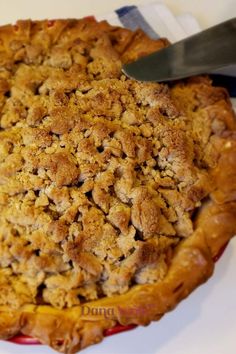 a pie with crumbs on top and a knife in the middle, ready to be eaten