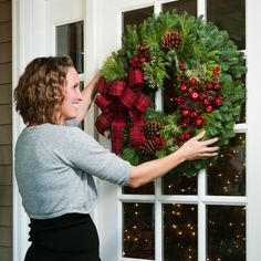 a woman is holding a christmas wreath on the front door to show it's holiday spirit