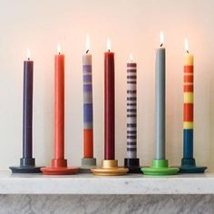 seven candles lined up on a mantle with one candle in the middle and another burning brightly