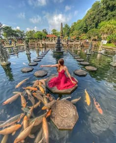 a woman in a red dress is sitting on a small boat surrounded by gold fish