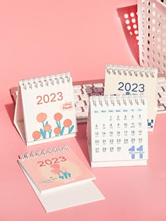 three calendars sitting next to each other on a pink surface