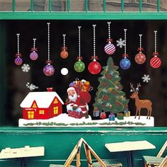 a window with christmas decorations on it and santa clause next to a tree in the snow