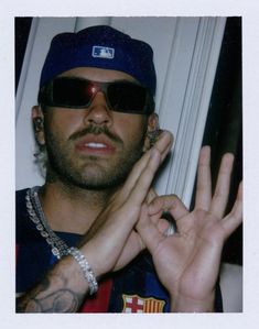 a man in sunglasses and a baseball cap making the v sign with his hands while wearing a hat