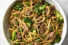 a white bowl filled with noodles, meat and broccoli on top of a table