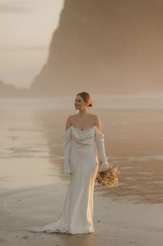 a woman standing on top of a beach next to the ocean wearing a white dress