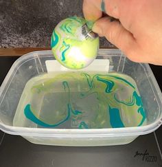 a hand is holding an object in a plastic container with blue and green swirled paint on it