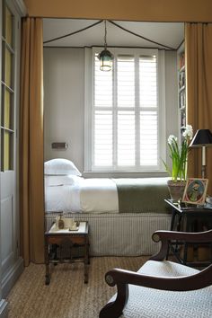 a bed sitting next to a window in a bedroom under a light fixture on top of a wooden table