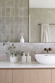 a bathroom sink sitting under a large mirror next to a white vase filled with flowers