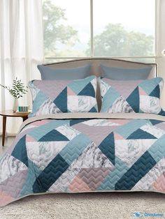 a bed covered in a blue, pink and white quilted comforter set next to a window