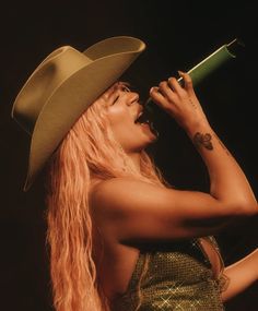 a woman with long hair wearing a cowboy hat and holding a microphone in her hand