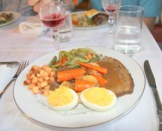 a white plate topped with meat and vegetables next to an egg on top of a table