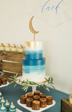 a blue and white cake sitting on top of a table next to cupcakes