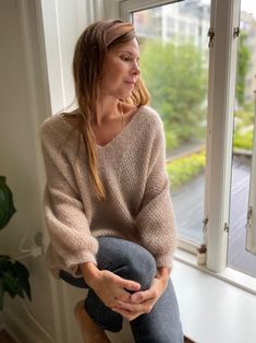 a woman sitting on top of a wooden chair next to an open window with a potted plant in front of her