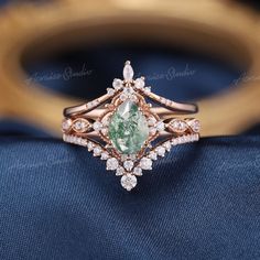 an engagement ring with green and white stones on it's side, sitting on top of a blue cloth