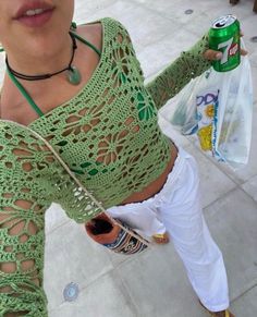 a woman in green shirt holding up a can of soda and wearing white pants with yellow shoes