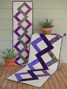 two quilts sitting on top of a wooden table next to a potted plant