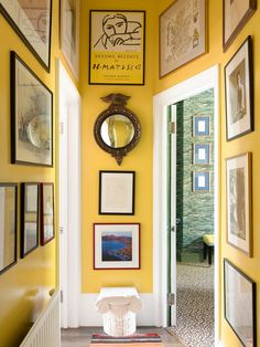 a hallway with yellow walls and framed pictures on the wall, along with a white toilet