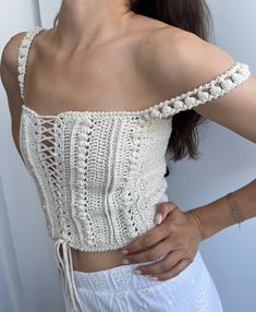 a woman wearing a white crochet top with her hands on her hips and looking at the camera