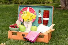 an open suitcase filled with food on top of a grass covered field next to trees