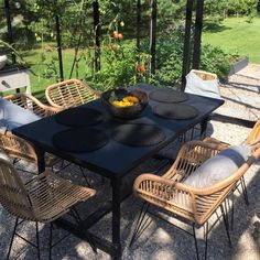 an outdoor dining area with wicker chairs and black table set for four, surrounded by greenery