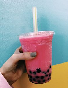 a hand holding a pink drink with black spots on the rim and straw in it