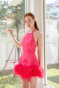 a woman standing in front of a window wearing a pink dress with ostrich feathers