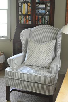 a chair with a pillow on top of it in front of a bookcase and window