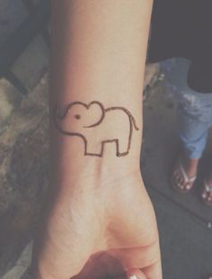 a small elephant tattoo on the wrist of a woman's hand with two fingers