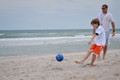 a father and son playing on the beach with a blue ball in front of them