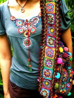 a woman wearing a gray shirt holding a multicolored purse and scarf in her hands