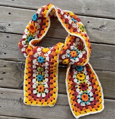 a multicolored crocheted scarf sitting on top of a wooden floor next to a piece of wood