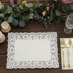 a place setting on a wooden table with white napkins and silverware, gold cutlery and flowers