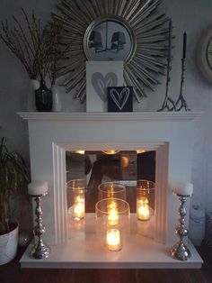 candles are lit in front of a fireplace with a mirror on the wall behind it