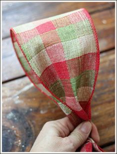 a hand holding a red and green checkered ribbon on top of a wooden table