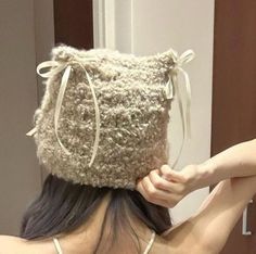 a woman wearing a knitted hat in front of a mirror with her hands on her head