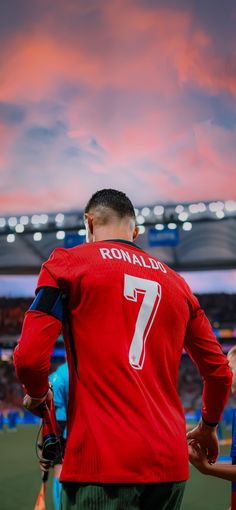 the back of a man in a red shirt at a soccer game with his hands on his hips