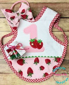 a pink and white bib with strawberries on it is sitting on a wooden surface