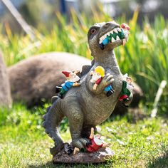 a toy dinosaur with toys on its back standing in the grass next to some rocks