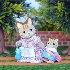 a cat and kitten doll sitting next to each other on the ground in front of trees