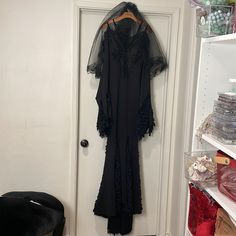 a black dress hanging on a door with a veil over it's head and shoes in the background