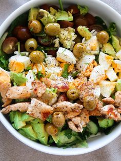 a salad with chicken and olives in a white bowl