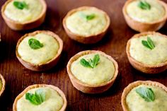 four small tarts with green leaves on top sitting on a wooden table next to each other