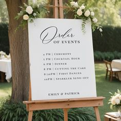 a sign with flowers on it sitting in front of a table at a wedding reception