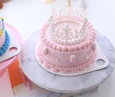 there is a pink cake with a crown on top and other cakes in the background