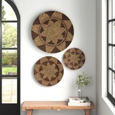 three woven circles hang on the wall next to a table with a potted plant