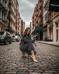 a woman kneeling down on the side of a brick road in front of tall buildings