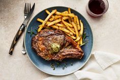 a steak and french fries on a blue plate next to a glass of red wine